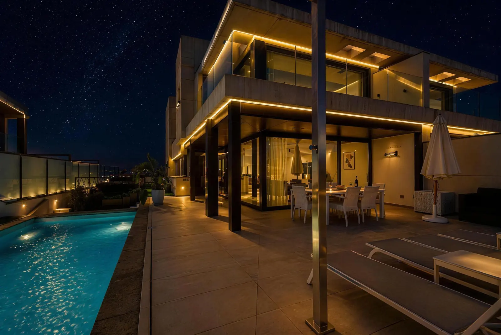 The villa at night with warm lights, porch dining area and lit pool
