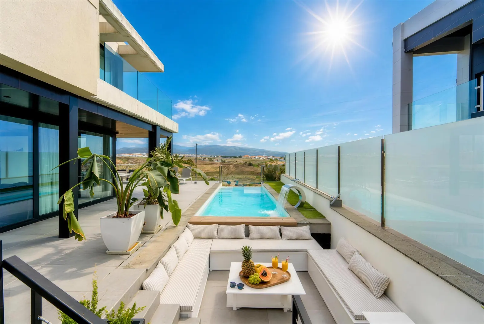 Sunken lounge with white cushions and fruit on the table, facing the private pool with waterfall and the mountains behind